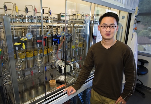 A young Yi Liu stands in front of a fume hood in a laboratory setting. 